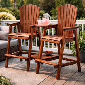 May include: Two wooden Adirondack-style bar stools with built-in side tables. The chairs are a warm brown color and have high backs with vertical slats. A pitcher of pink lemonade and glasses sit on the side tables. A small bowl of red fruit is on the lower shelf.