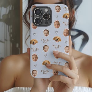 May include: A pale blue phone case with a repeating pattern of baby faces, golden retrievers, and hearts. The text "I love You Dad!" is printed across the design. The case is designed for a smartphone.