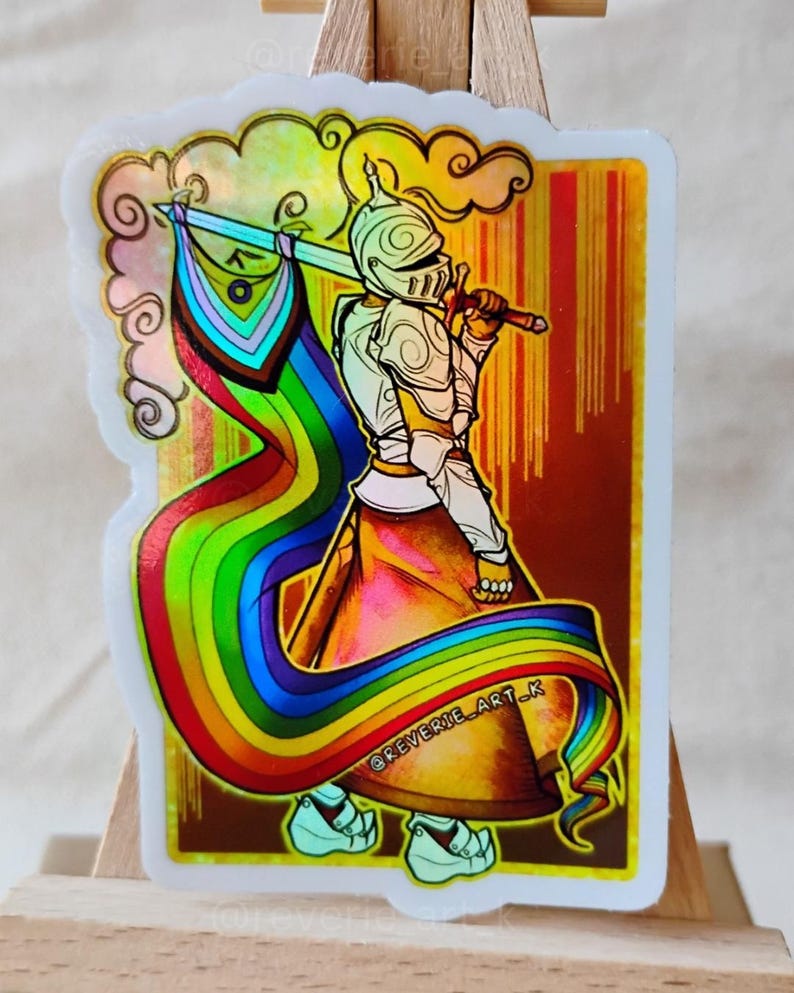 May include: A sticker featuring a knight in shining armor holding a sword and a rainbow flag. The knight is depicted with a helmet and armor, and the flag flows behind them. The sticker has a holographic effect and the text "@reverie_art_k".