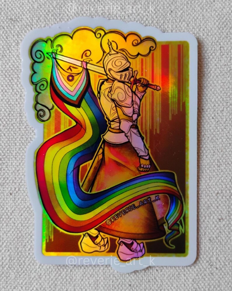 May include: A sticker featuring a knight in golden armor holding a sword with a rainbow flag. The knight is set against a gold background with a rainbow ribbon flowing from the flag. The sticker has the text "@reverie_art_k".