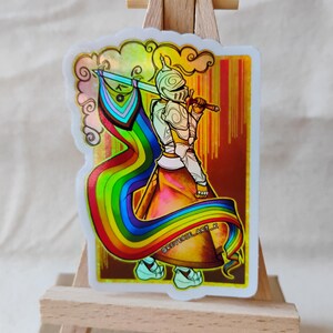May include: A holographic sticker featuring a knight holding a rainbow flag and sword. The knight is wearing armor and a helmet. The sticker has a white border with a cloud design. The background is a gradient of gold and brown.