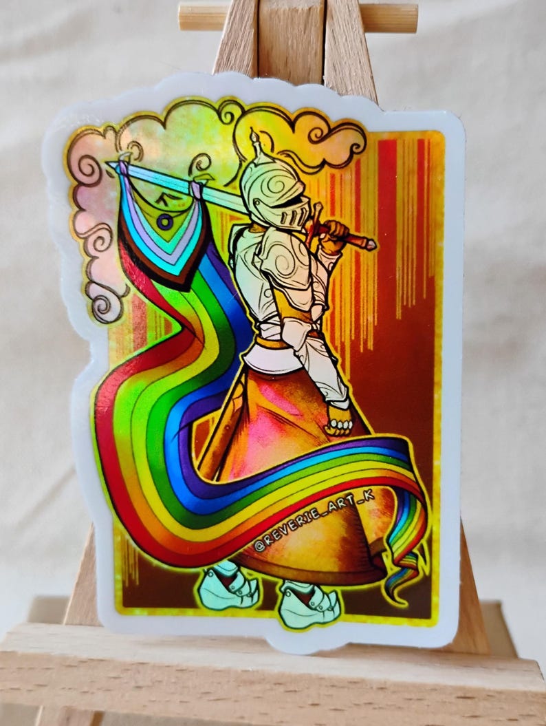 May include: A sticker featuring a knight in silver armor holding a sword and a rainbow flag. The sticker has a holographic effect with a gold border and the text "@REVERIE_ART_K". The knight is set against a gradient background.