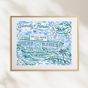 May include: Framed art print featuring the University of Florida's Ben Hill Griffin Stadium. The artwork showcases the stadium in blue and green hues, with the text "University of Florida" and a gator illustration. The print is framed in a gold-colored frame.