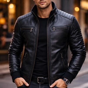 Könnte beinhalten: Schwarze Lederjacke mit geripptem Kragen und Schulterdetails. Die Jacke hat mehrere Reißverschlusstaschen und einen Frontreißverschluss. Die Person trägt ein schwarzes T-Shirt, eine dunkelblaue Jeans und einen schwarzen Gürtel. Die Person trägt auch eine Sonnenbrille und eine Uhr.