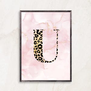 May include: Framed art print featuring the letter "U" in a black and gold leopard print design. The background is a soft pink watercolor with gold accents. The frame is a dark brown color.