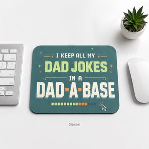 May include: A rectangular dark green mouse pad featuring the text I KEEP ALL MY DAD JOKES IN A DAD-A-BASE in light green and white block lettering. The design includes small star accents, horizontal lines, and a loading bar with a cursor icon.