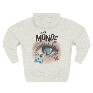 Peut inclure: Un sweat à capuche gris chiné clair avec un motif au dos. Le dessin représente un grand œil humain dont l'iris est un globe terrestre tenu par une main. Au-dessus de l'œil, le texte UN SEUL MONDE, et en dessous, un symbole de recyclage et ESPOIR.