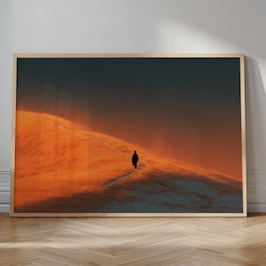 May include: A framed print featuring a solitary figure walking along a path on a sunlit hillside. The artwork showcases a warm color palette of orange and gold, with a dark, moody sky. The person is silhouetted against the bright landscape.