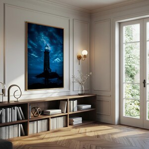 Puede incluir: Una impresión enmarcada de un faro bajo un cielo azul oscuro y dramático. La obra de arte cuelga sobre una estantería de madera llena de libros. La habitación cuenta con apliques de pared y una gran ventana.
