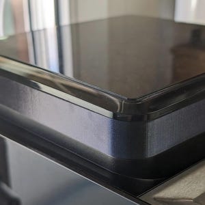 May include: A close-up shot of a black, rectangular item with rounded corners. It has a shiny, reflective surface and a dark, textured border. The image is well-lit, showing the details of the object's design and build.