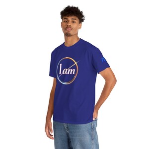 Peut inclure: T-shirt bleu roi avec l'inscription "I am" dans un cercle blanc, doré et argenté sur le devant. Le t-shirt a des manches courtes et un col rond. Les lettres "TI" sont sur la manche droite.