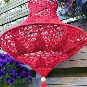 May include: A red crocheted lampshade with a wooden bead and tassel hanging from the bottom.