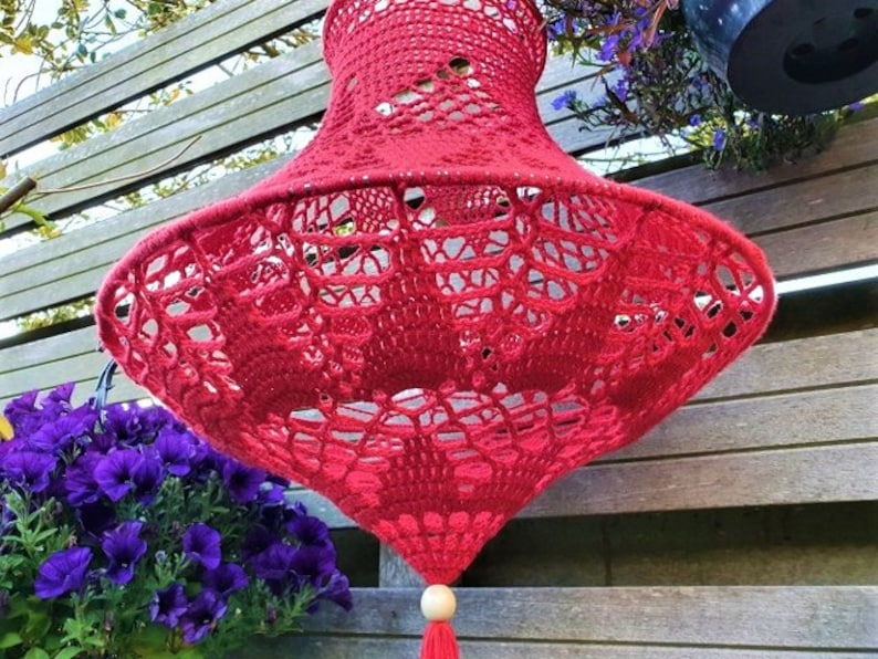 May include: A red crocheted lampshade with a wooden bead and tassel hanging from the bottom.