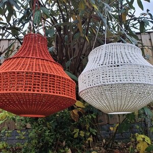 May include: Two hanging light fixtures, one orange and one white, are made of woven rope and have a round, bell-shaped design.