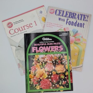 May include: Three Wilton cake decorating books. The titles include "Course 1", "Celebrate! With Fondant", and "Beautiful Gum Paste Flowers". The "Beautiful Gum Paste Flowers" book features a floral arrangement on the cover.