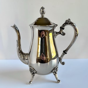 Cafetera antigua de plata con patas ornamentadas con motivos florales, servidor de té y elegante pieza de exhibición.