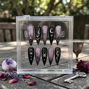 May include: A set of ten stiletto-shaped press-on nails displayed in a clear plastic case. The nails feature a black and muted purple gradient color scheme with silver metallic accents including spider webs, spiders, flames, stars, and moons.