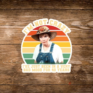 May include: A sticker featuring a woman wearing a straw hat and denim overalls, set against a retro sunset design. The text reads "I'M NOT CRAZY, I'VE JUST BEEN IN A VERY BAD MOOD FOR 40 YEARS."