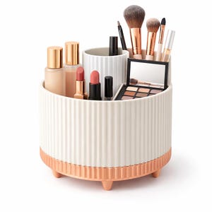 Peut inclure: Un organisateur de maquillage blanc et or rose avec un design côtelé. L'organisateur contient divers cosmétiques, notamment des rouges à lèvres, des flacons de fond de teint, des pinceaux de maquillage et une palette de fards à paupières. Il est rond et surélevé par de petits pieds.