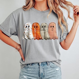 May include: A grey short-sleeve t-shirt featuring a graphic print of four ghosts arranged in a row. Each ghost has a distinct pattern: one with orange floral print, one with solid orange, one with beige gingham, and one with orange gingham.