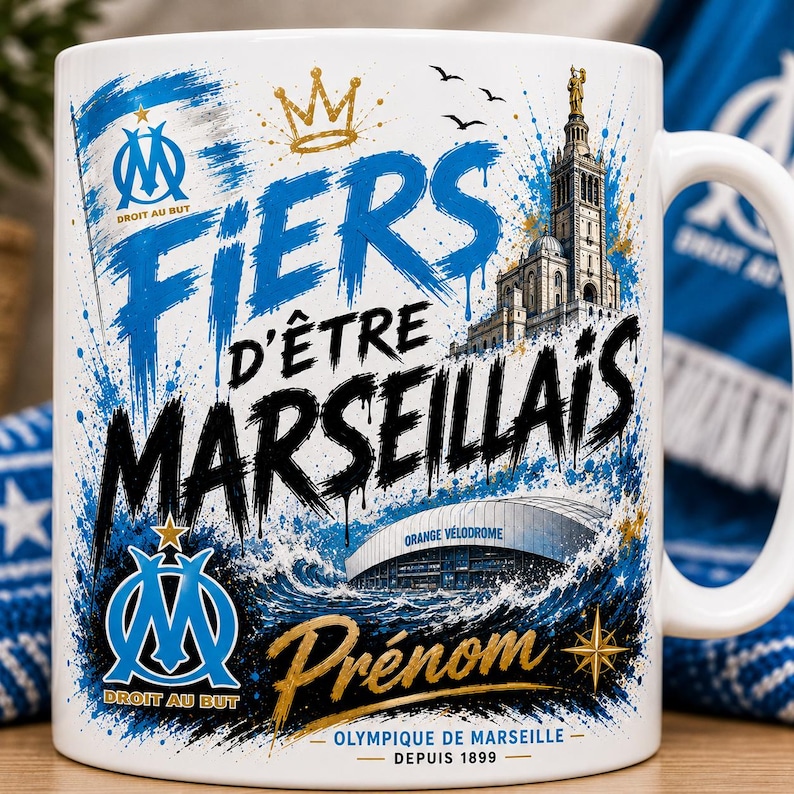 May include: A white ceramic mug featuring blue and black graphic designs, including the text FIERS D'&Ecirc;TRE MARSEILLAIS, the Olympique de Marseille logo, the Orange V&eacute;lodrome stadium, the Notre-Dame de la Garde basilica, and the word Pr&eacute;nom.