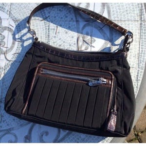 Könnte beinhalten: Schwarze Umhängetasche mit braunem Zierbesatz und einer plissierten Vordertasche. Die Tasche hat einen Reißverschluss und einen braunen Griff. Die Tasche ist aus Nylon.