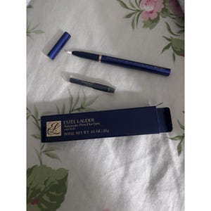 May include: An Estée Lauder automatic eye pencil set. The set includes a navy blue pencil with a cap, a refill pencil, and a navy blue box. The box has the Estée Lauder logo and product information printed on it.