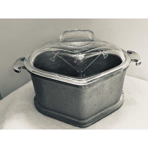 Puede incluir: Una fuente para horno gris vintage con tapa de cristal transparente. La tapa presenta diseños grabados y un asa. La fuente tiene un exterior texturizado y asas laterales. Un artículo de cocina clásico.