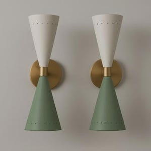 May include: Two mid-century modern wall sconces. Each sconce features a white, cone-shaped top with small perforations, a brass-colored central section, and a green, cone-shaped bottom. The sconces are mounted on round, brass-colored backplates.