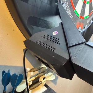 Pu&ograve; includere: Un bersaglio elettronico nero con il logo Target. Il bersaglio &egrave; montato a parete e presenta un design geometrico nero. Sono visibili diverse freccette, alcune blu e altre con punte metalliche.