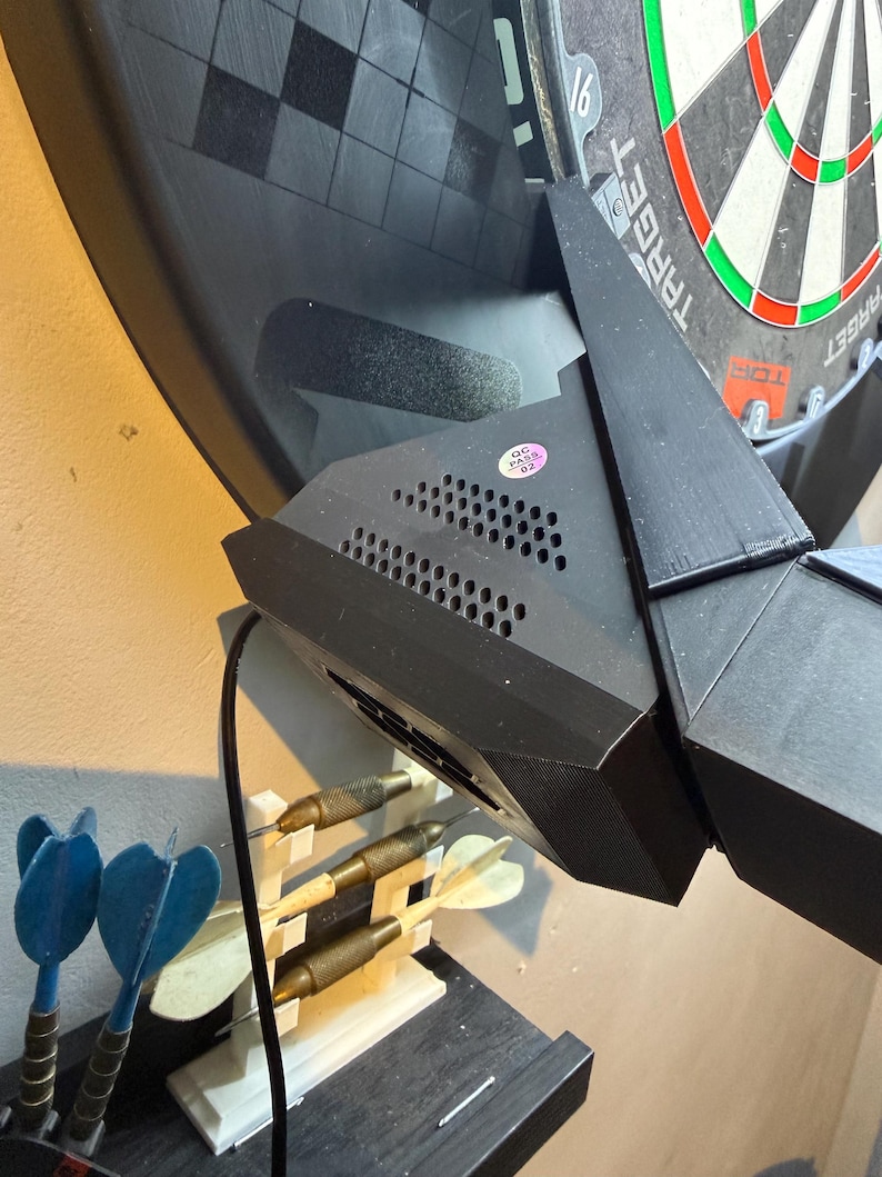 Pu&ograve; includere: Un bersaglio elettronico nero con il logo Target. Il bersaglio &egrave; montato a parete e presenta un design geometrico nero. Sono visibili diverse freccette, alcune blu e altre con punte metalliche.