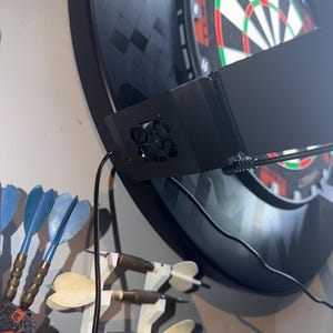Pu&ograve; includere: Un bersaglio elettronico nero con una cornice nera, un'unit&agrave; di punteggio elettronica nera e un set di freccette blu e ottone. Il bersaglio &egrave; montato su una parete di colore chiaro. Freccette aggiuntive sono esposte su un supporto bianco.