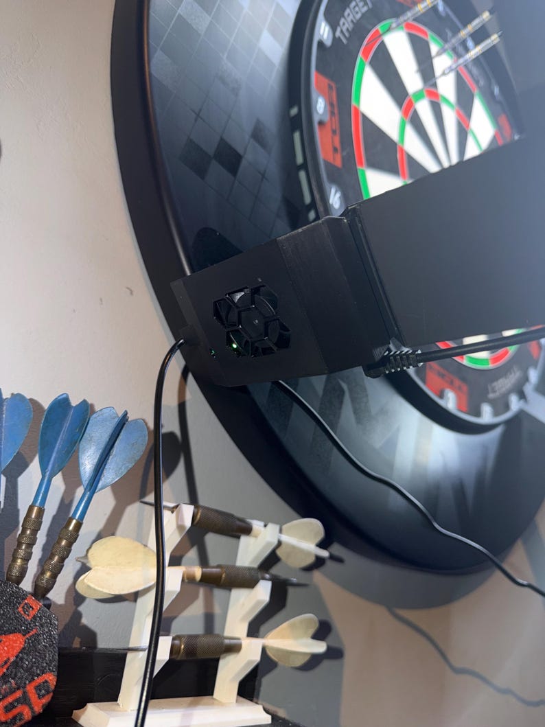 Pu&ograve; includere: Un bersaglio elettronico nero con una cornice nera, un'unit&agrave; di punteggio elettronica nera e un set di freccette blu e ottone. Il bersaglio &egrave; montato su una parete di colore chiaro. Freccette aggiuntive sono esposte su un supporto bianco.