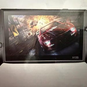 以下が含まれることがあります： レース中の赤いスポーツカーを表示する画面を備えた黒い携帯ゲーム機。コンソールにはボタン、方向パッド、下部に「X13S」という文字があります。