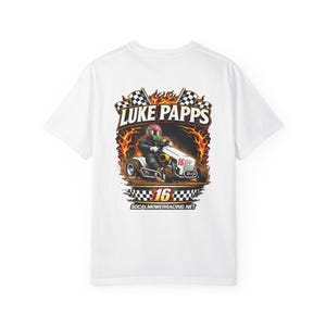 May include: White t-shirt featuring a colorful graphic of a person racing a lawnmower. The design includes the text "LUKE PAPPS" above the image, with the number "16" and "SOCALMOWERRACING.NET" below.