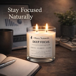 May include: A lit, clear glass candle labeled "DEEP FOCUS" sits on a desk. The candle has two wicks and is surrounded by a notebook, pen, and a laptop. The text "Stay Focused Naturally" is at the top of the image.