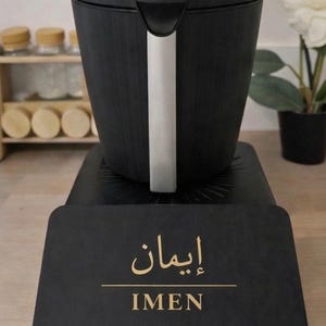 May include: Black electric kettle with a silver handle and a black base. The base has the name "IMEN" in gold lettering. The kettle is on a black surface.