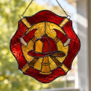 May include: A stained glass suncatcher shaped like a Maltese cross, featuring a central red firefighter helmet and two crossed axes over a yellow background. The outer border is deep red, and the entire piece hangs from a metal chain.