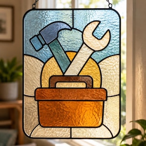 May include: A rectangular stained glass suncatcher featuring a central orange toolbox with a brown handle. Inside the toolbox are a blue hammer and a white wrench. The background consists of a yellow sun shape set against a light blue sky.