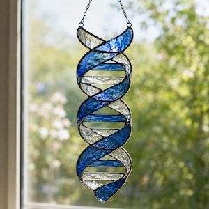 Könnte beinhalten: Ein Buntglas-Sonnenfänger in Form einer DNA-Doppelhelix. Das Objekt besteht aus abwechselnden Segmenten aus texturiertem kobaltblauem und klarem, irisierendem Glas, die durch dunkle Metalllötstellen verbunden und an einer dünnen Metallkette aufgehängt sind.