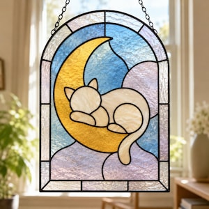 Peut inclure: Un capteur de soleil en vitrail arqué représentant un chat blanc recroquevillé sur un croissant de lune jaune. Le fond est composé de panneaux de verre texturés bleus et violet clair. L'ensemble est encadré de métal noir et suspendu par une chaîne.