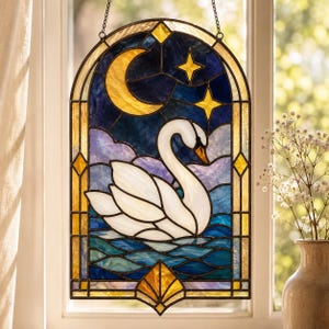 Peut inclure: Panneau de fenêtre en vitrail représentant un cygne sur l'eau sous un croissant de lune et des étoiles. Le panneau a un sommet en arc de cercle bleu foncé et doré et un fond décoratif. Le cygne est blanc avec un bec orange, et l'eau est bleue et verte.