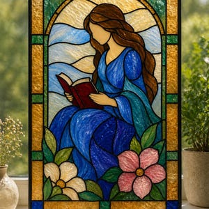 Può includere: Pannello in vetro colorato raffigurante una donna in abito blu che legge un libro. L'opera d'arte include un disegno floreale con fiori rosa e bianchi, su uno sfondo di tonalità blu e oro. Il pannello è incorniciato in nero.