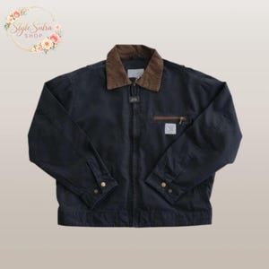 Op de afbeelding: Een marineblauwe jas met een bruine kraag en een ritssluiting. De jas heeft een klein borstzakje en manchetten met knopen. De jas heeft een label en een kleine witte vierkante patch. De jas is van Style Sutra Shop.