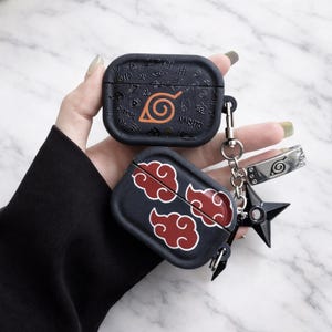 May include: Two black AirPod cases with Naruto-themed designs. One case features an orange spiral symbol and the word "NARUTO". The other case has red cloud graphics. A silver keychain with a shuriken and a headband charm is attached.