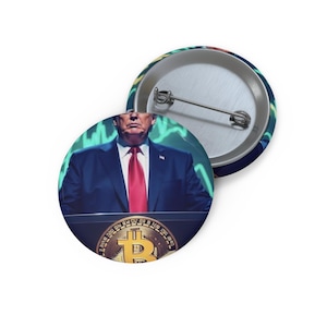May include: A circular pin-back button featuring a graphic of a person in a dark blue suit and red tie standing behind a podium with a gold Bitcoin logo. The background displays green financial chart lines. The back shows a silver metal pin mechanism.