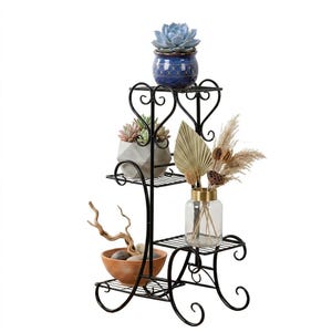 May include: A three-tiered black metal plant stand with decorative scrollwork. The stand holds various plants and decorative items, including succulents in ceramic pots, dried flowers in a glass vase, and a terracotta bowl with stones and driftwood.