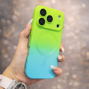 May include: A green and blue gradient phone case. The case features a raised camera module with three lenses and a circular design. The case is designed to protect the phone and improve its look. The case is likely made of plastic.