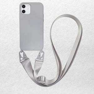 May include: A light gray smartphone case with a dual-camera cutout and a matching adjustable woven strap. The strap is attached to the bottom of the case with two metal carabiner-style clips, allowing the device to be worn around the body.