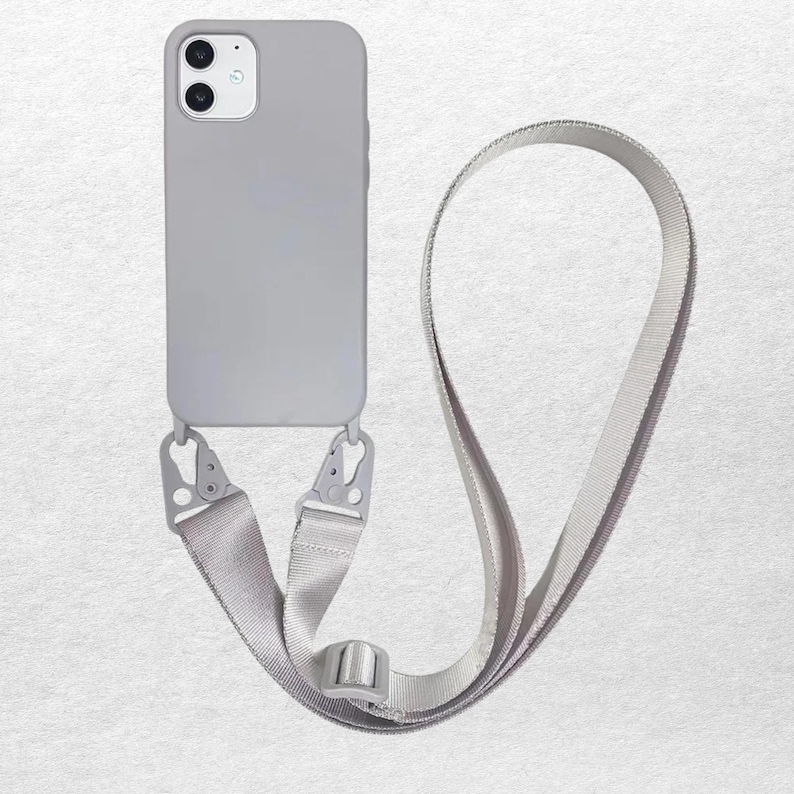 May include: A light gray smartphone case with a dual-camera cutout and a matching adjustable woven strap. The strap is attached to the bottom of the case with two metal carabiner-style clips, allowing the device to be worn around the body.